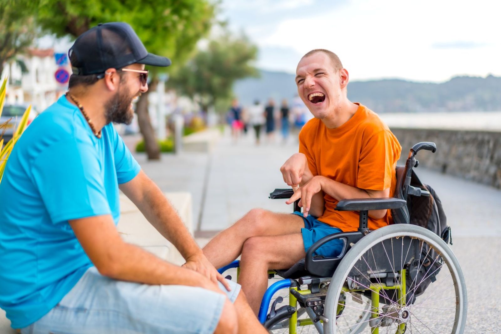 Man on a bench with a man in a wheelchair on a walkway by a waterfront.